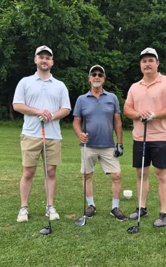 Gary Roberts standing on a golf course between his two grandsons, each holding a golf club.